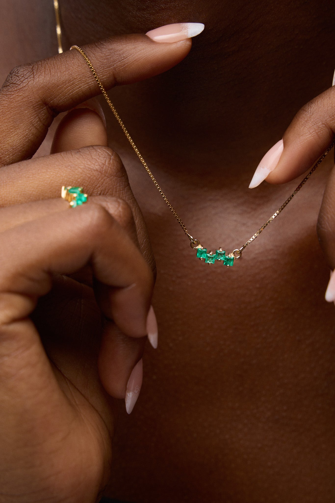 Close-up of a gold necklace with green gemstones being worn by a person.