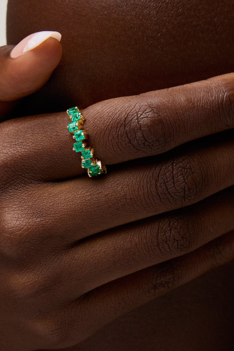 Hand wearing a green emerald ring on a neutral background